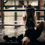 A female boxer sitting in a gym ring, resting and wiping sweat with a towel after a workout.